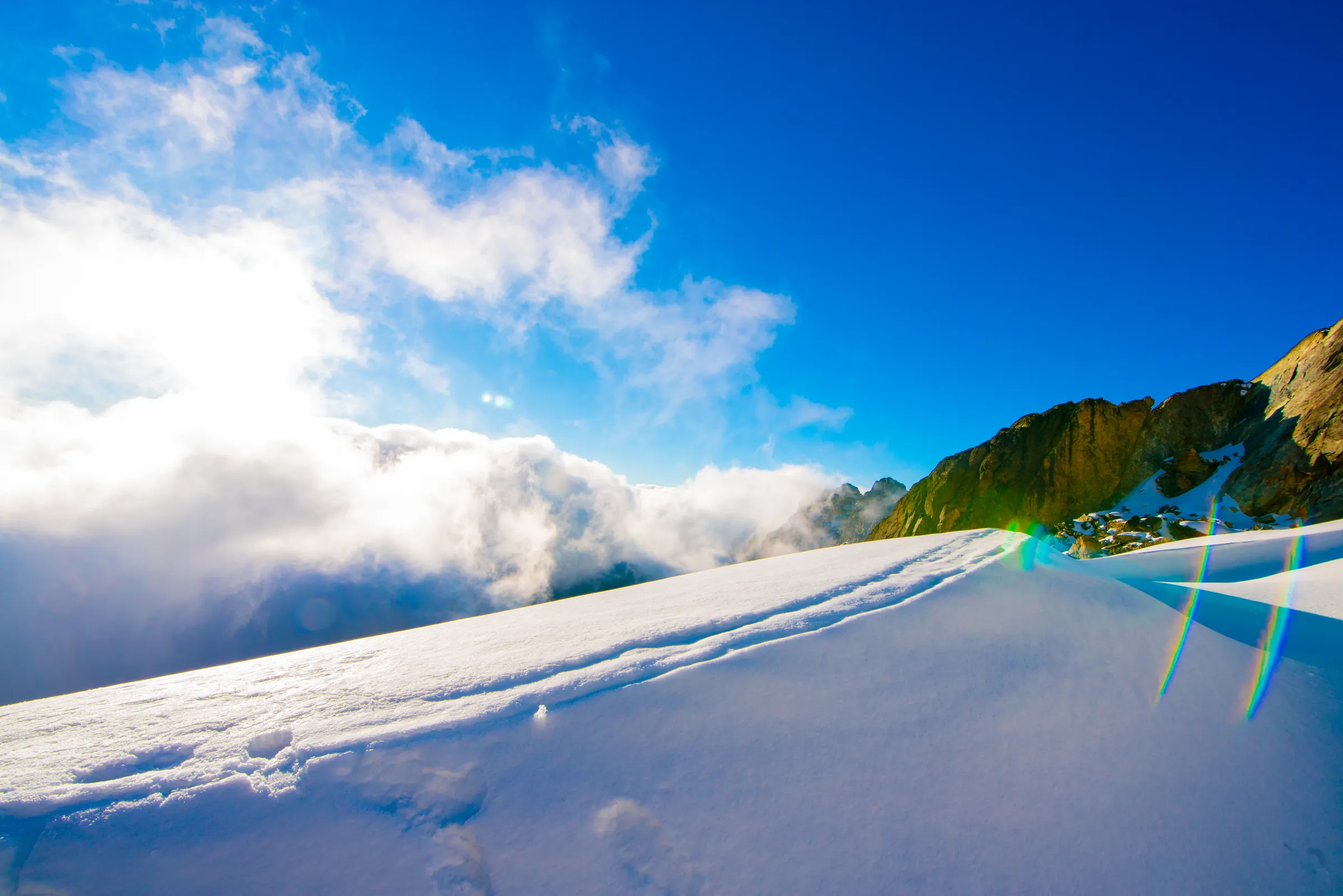 Footprints running along a wind-sculpted snow crest on the Rwenzori, with cloud banked against the ridge beyond